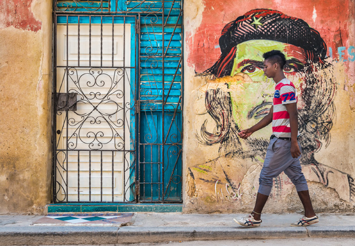 HAVANA,CUBA - MAY 20,2015 : Young cuban man walks by a colorful Che Guevara portrait painted on a shabby old wall in Old Havana